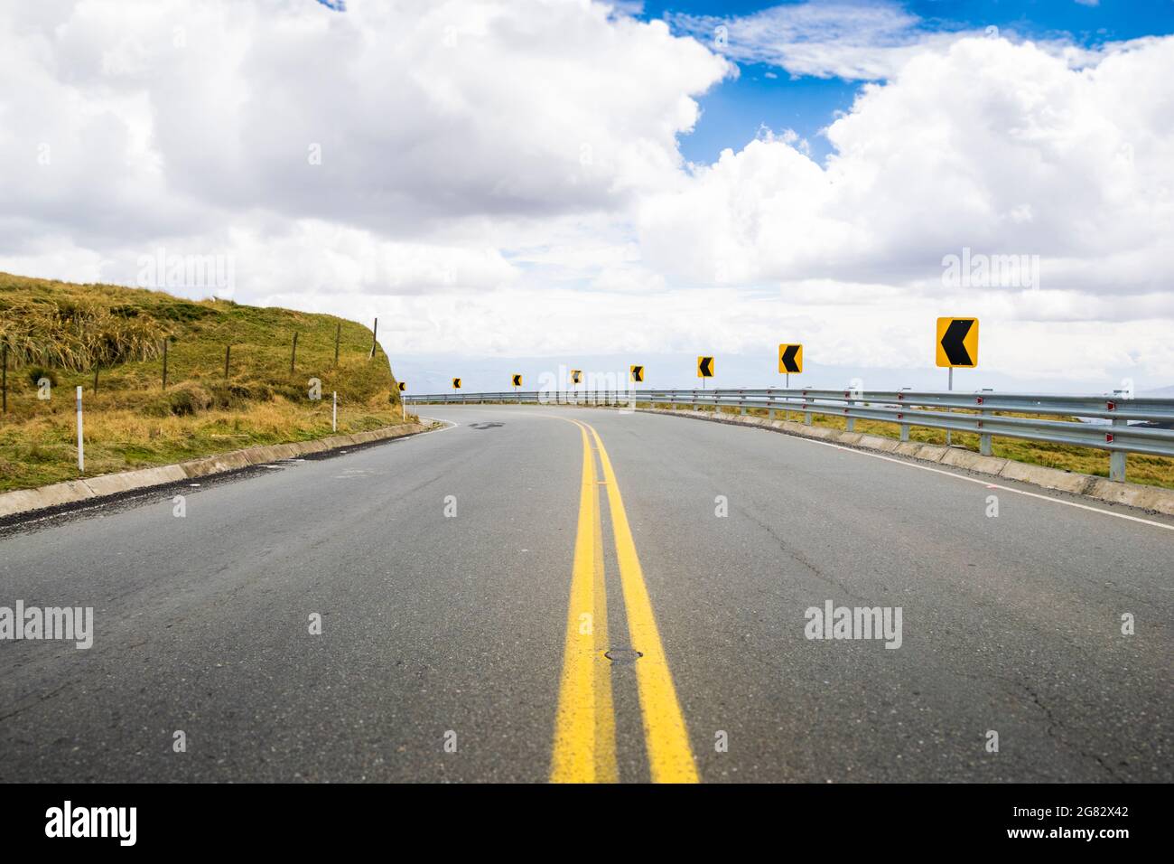 Highway in the mountains with a blue sky with some clouds. Street signs that indicate a curve. Stock Photo