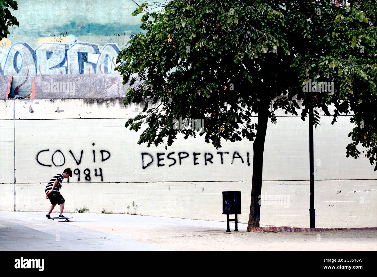 Teenage boy skateboarding in front of Covid-19 graffiti, Barcelona, Spain. Stock Photo