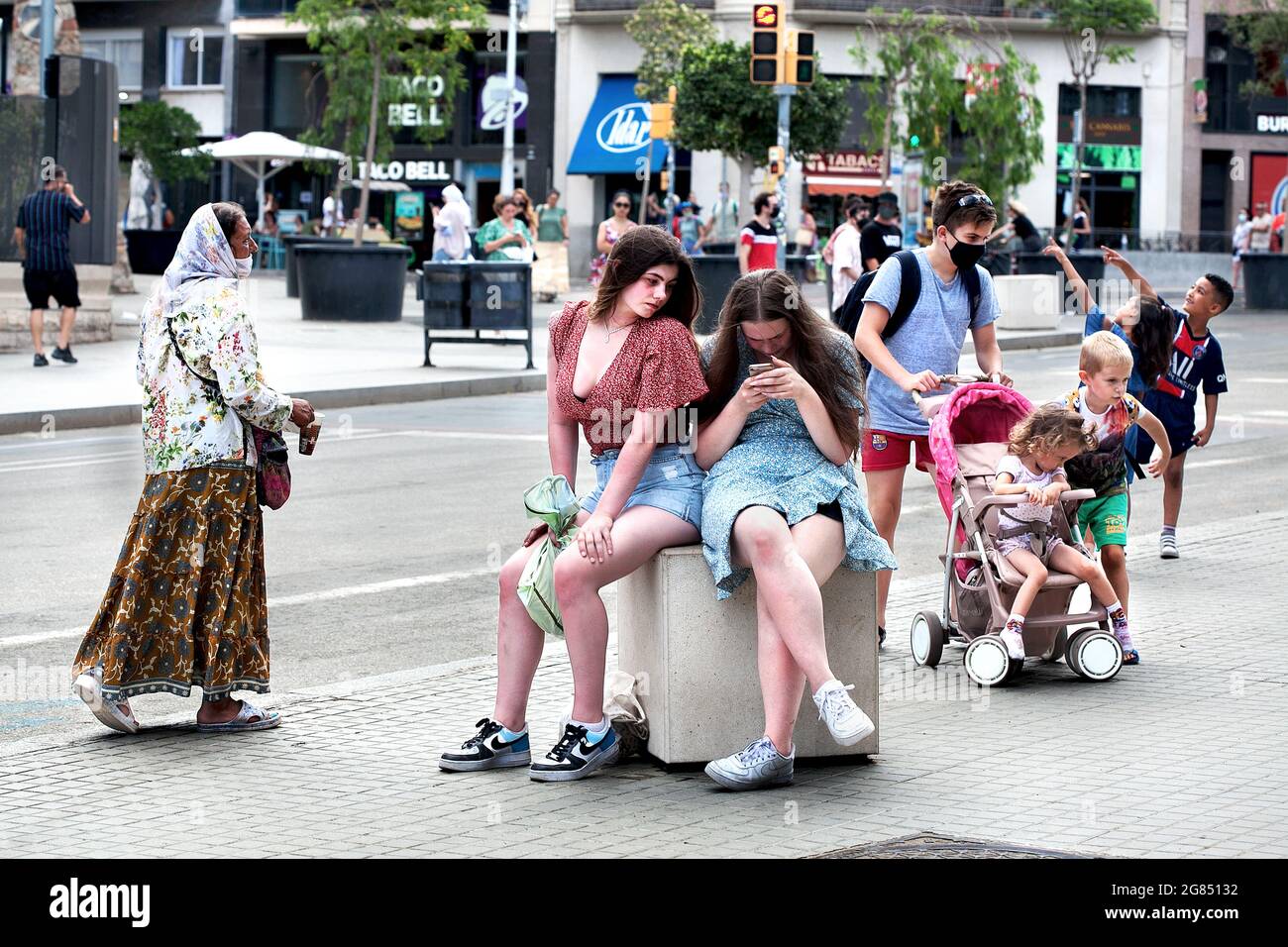 Teenage girls looking at their selfies and a Romanian gypsy woman on the prowl, Sagrada Familia, Barcelona, Spain. Stock Photo