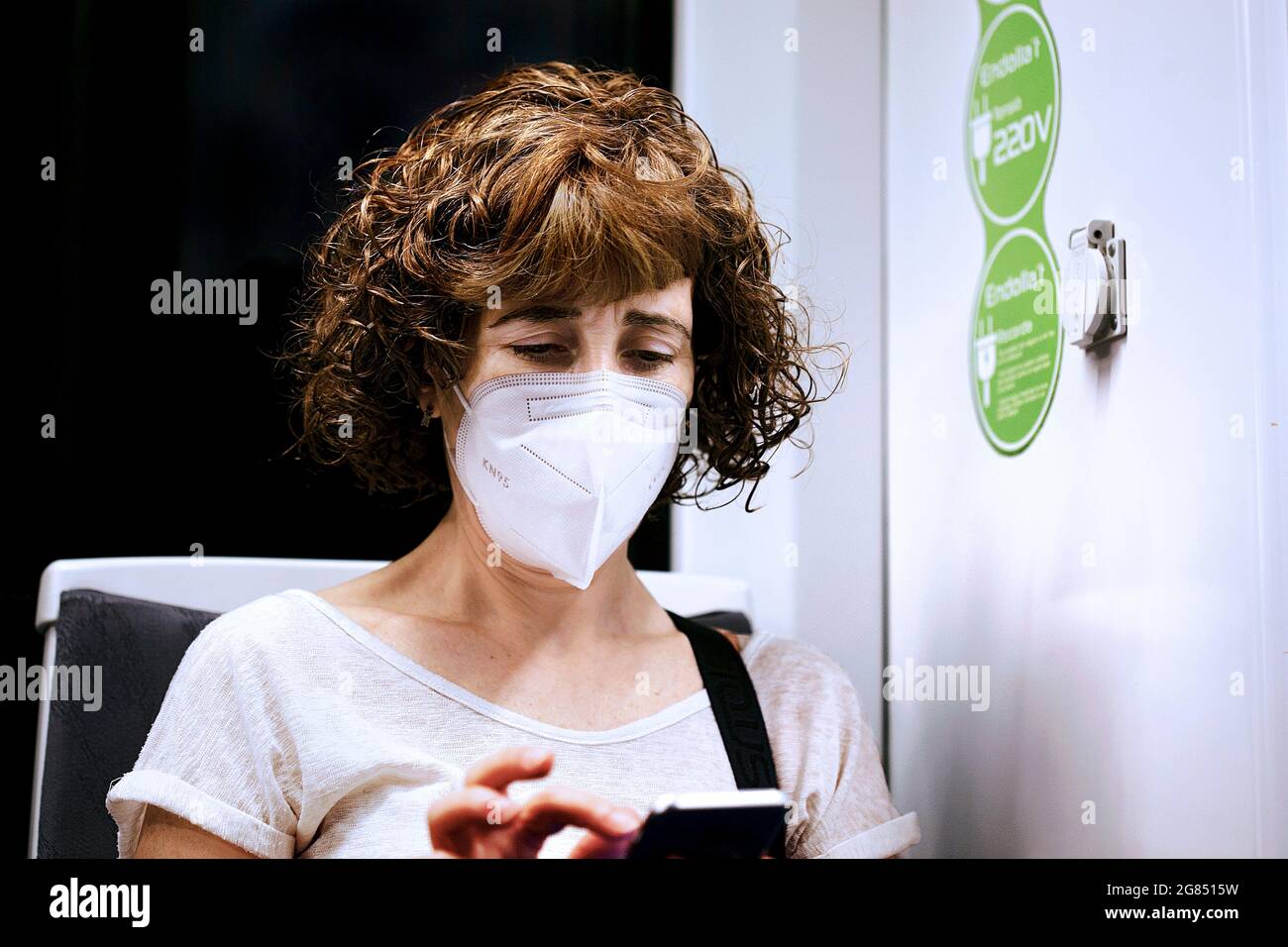Woman sat on train wearing mandatory face mask looking at her mobile