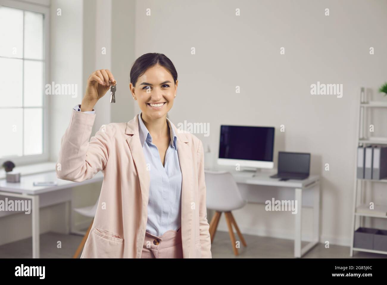 Happy real estate agent standing in office, holding keys to new house