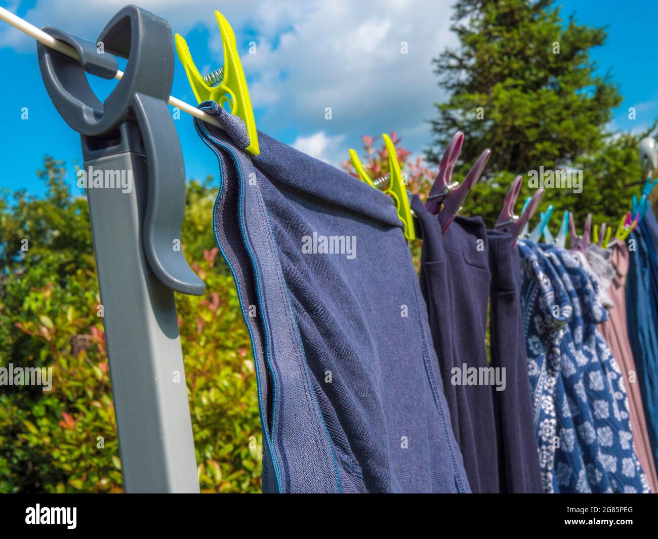Closeup POV shot of a prop / pole hooked onto a washing line, with pegged clothes hanging to dry in the sunshine, with bushes and a tree behind. Stock Photo