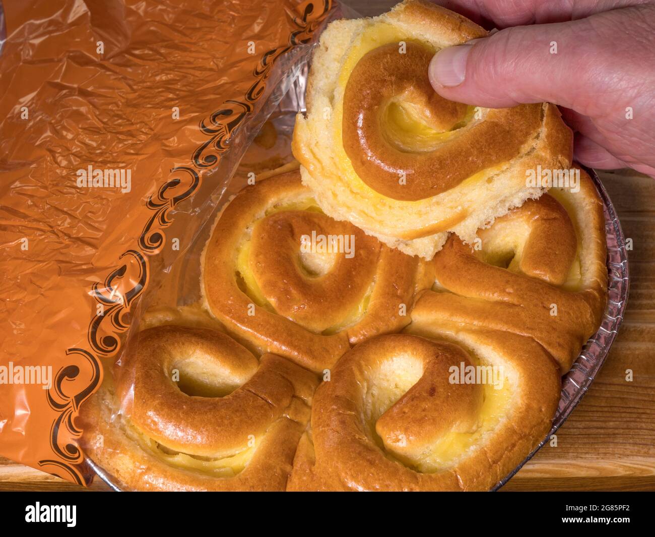 A man’s hand tearing off a piece of baked, soft, traditional French brioche bread, with a custard filling, taken from a tray in a retail packet. Stock Photo