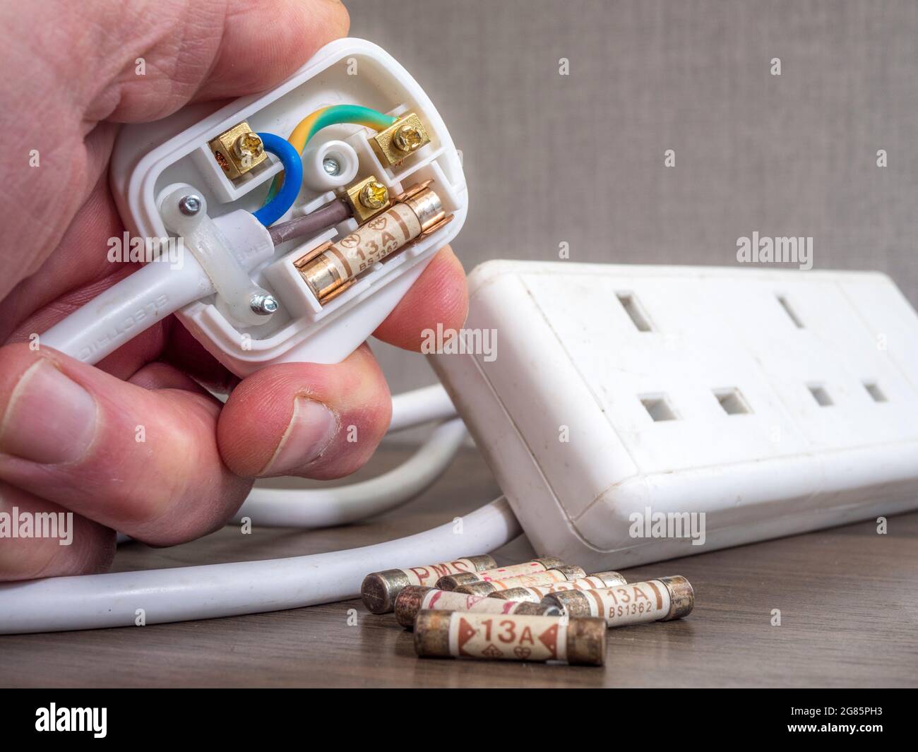 Closeup of a man’s hand holding an open three pin British electrical plug on the end of an extension lead, with new 13 amp fuses nearby. Stock Photo
