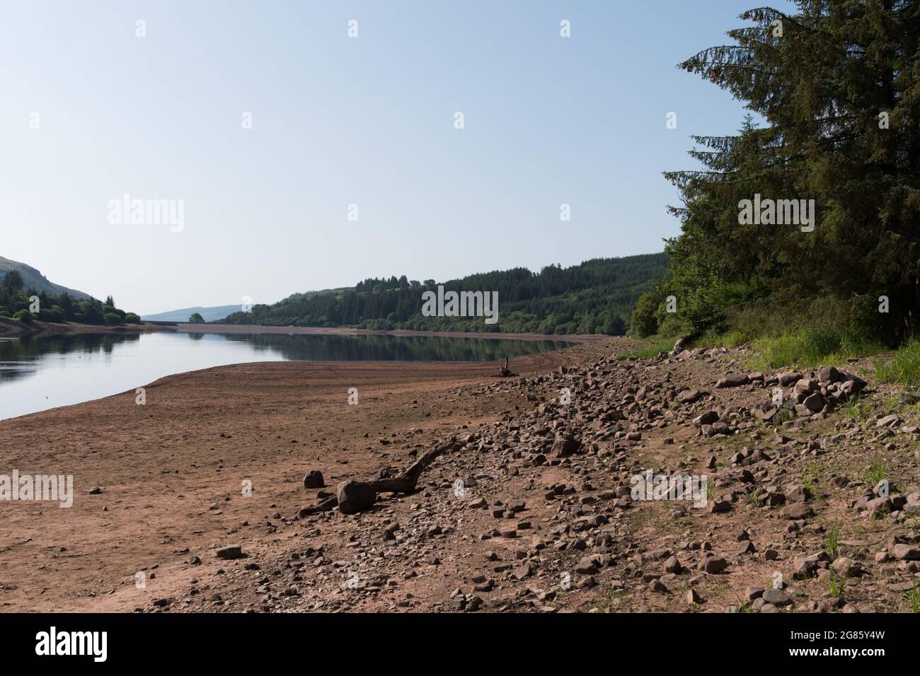 Llwyn Onn reservoir, Merthyr Tydfil, South Wales, UK.  17 July 2021.  UK weather:  Continued hot weather has lowered water levels at this reservoir and uncovered Pont Yr Daf bridge, normally underwater.  The bridge was in use before the reservoir was constructed. Credit: Andrew Bartlett/Alamy Live News Stock Photo