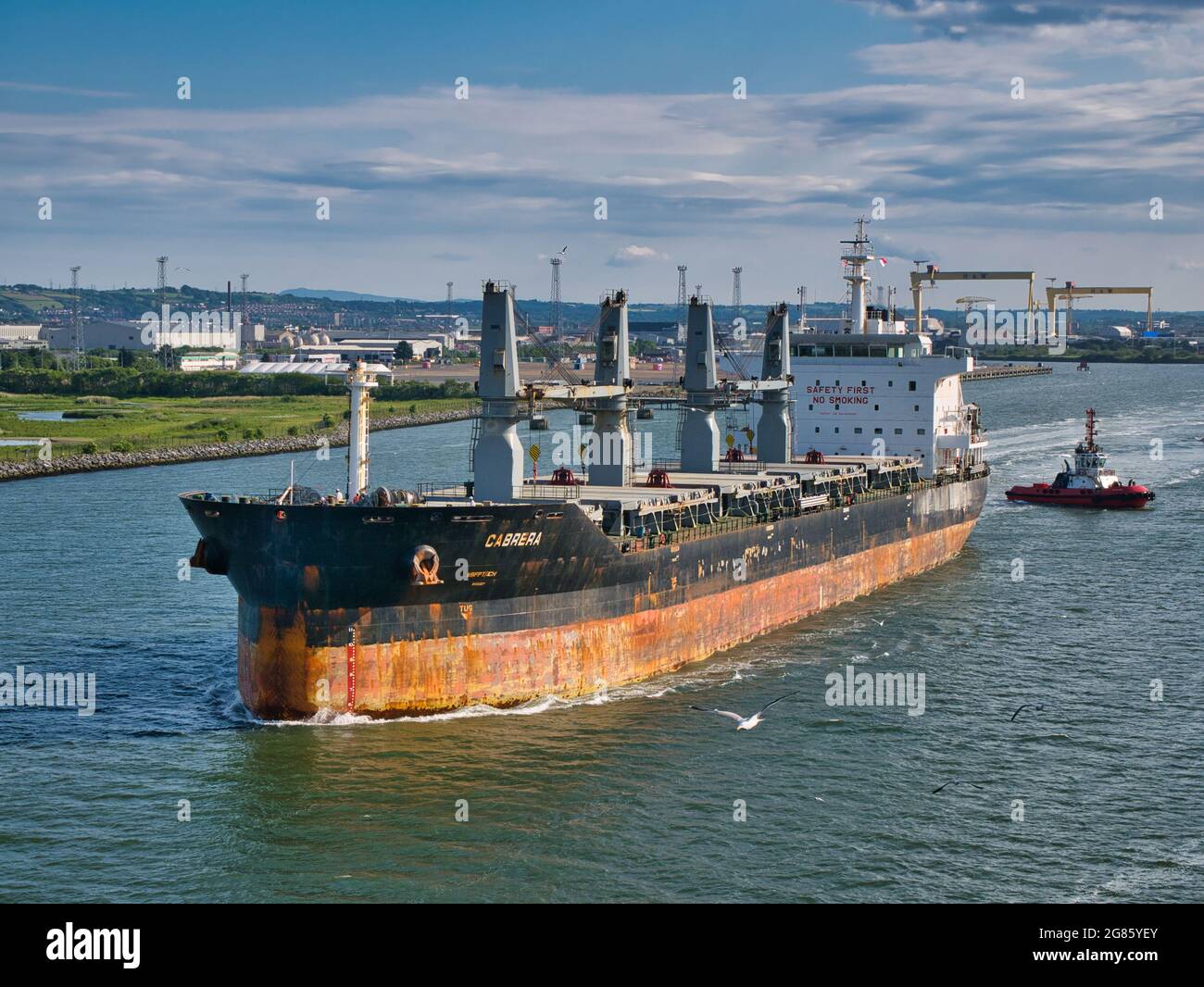The bulk carrier Cabrera leaving Belfast Harbour in June 2021 on a clear, sunny evening in June 2021. The ship is escorted by the Masterman tug boat. Stock Photo