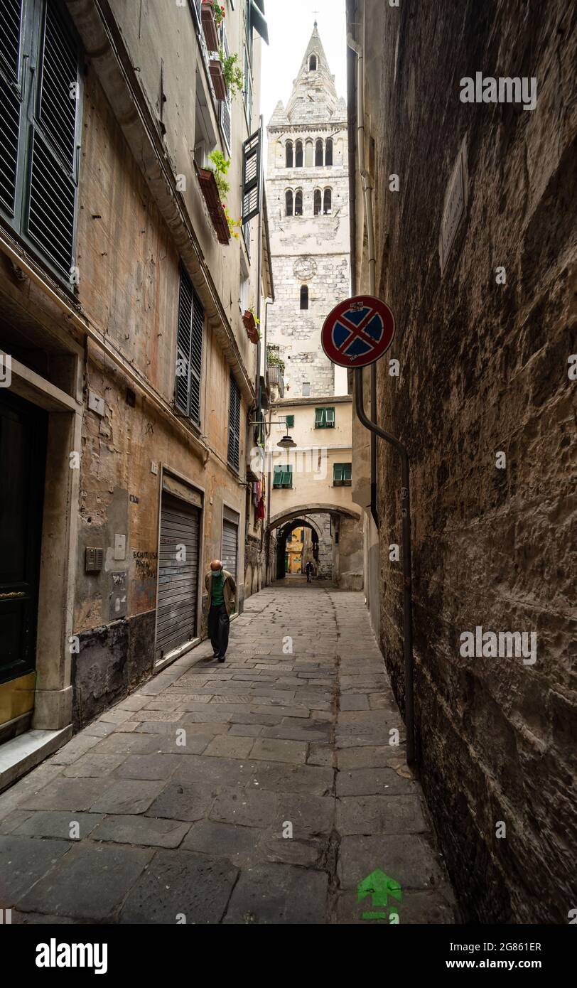 A 'caruggio' narrow alley in the historic centre of Genoa, Italy, with an old man and the bell tower of the Basilica di Santa Maria delle Vigne church Stock Photo