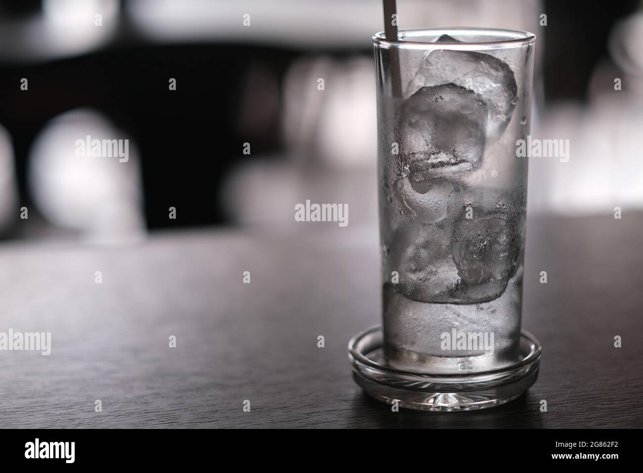A glass full of partially melted ice cubes, with a drinking straw, on a wooden table in coffee-shop Stock Photo