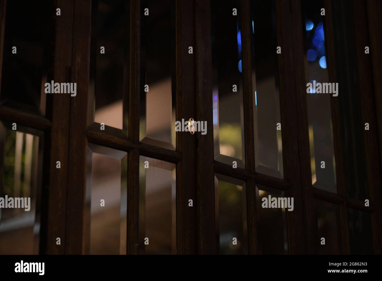A good-looking old-fashioned windows of thick glass and dark wood are reflecting street lights during another lockdown-night in an empty Pattaya hotel Stock Photo