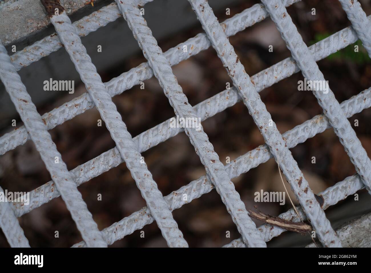 A mesh, made of metal rods, is covering a storm sewer channel on a sidewalk of public park Stock Photo