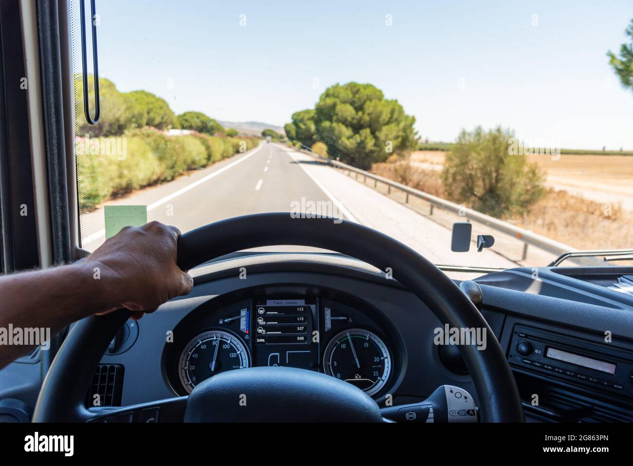 View that a truck driver has from his workplace, with one hand gripping the steering wheel, the dashboard with job information and the road in the bac Stock Photo