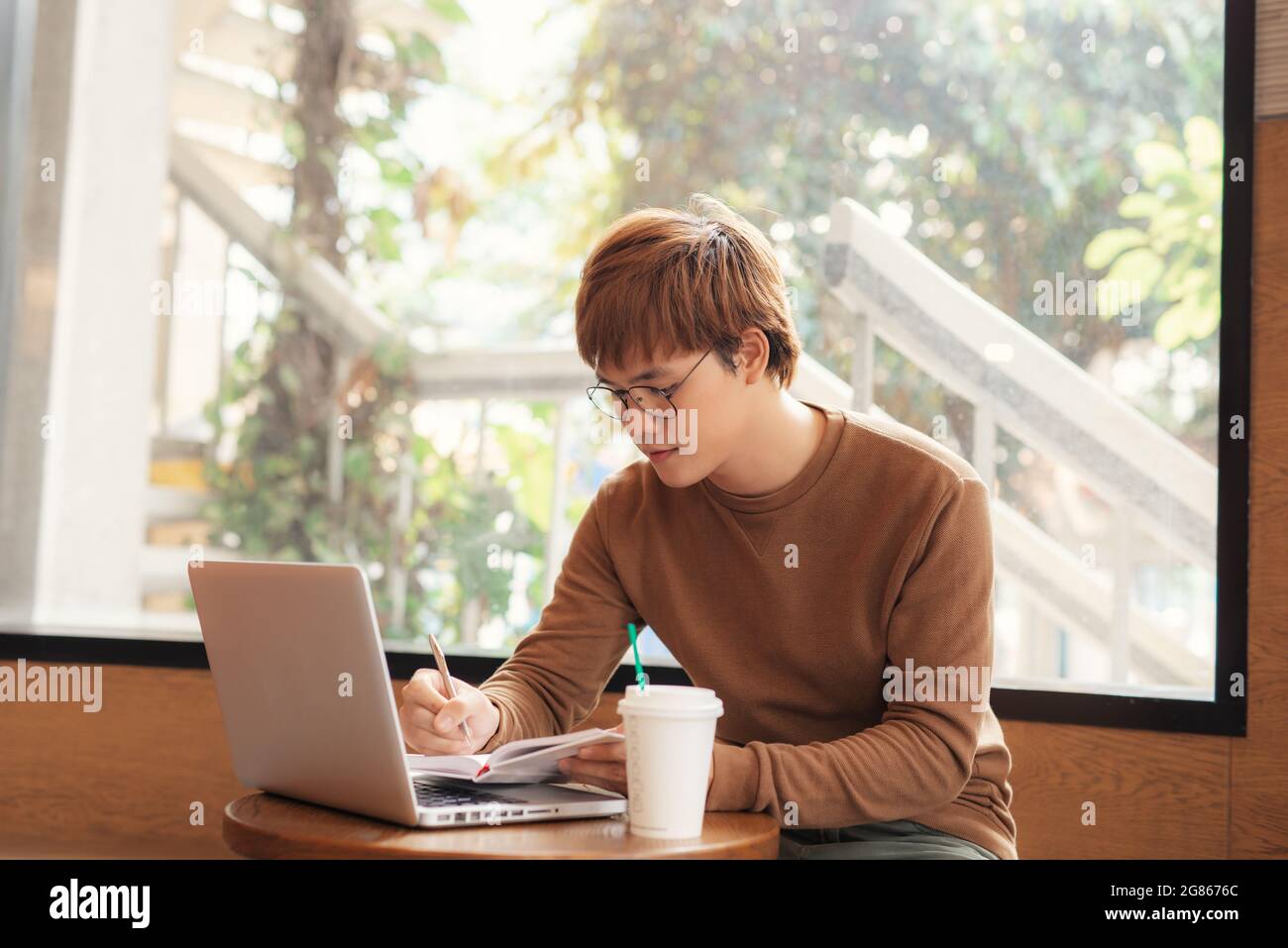 Focused millennial student making notes writing down information from book in cafe preparing for test Stock Photo