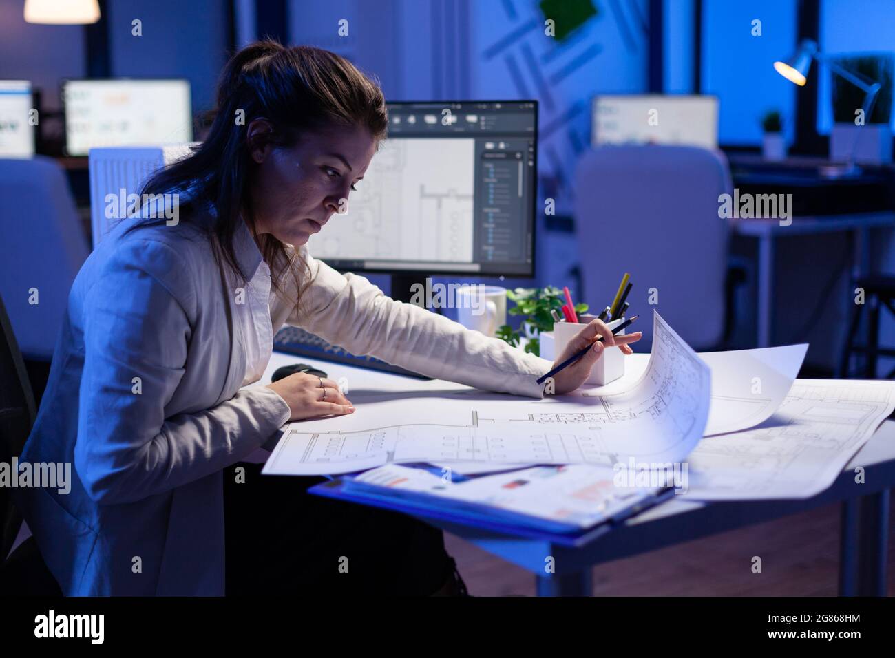 Over the shoulder shot of engineer woman drawing architectural plans and looking at cad software on desktop computer. Designer using arhitecture blueprints of buildings creating industrial prototype Stock Photo