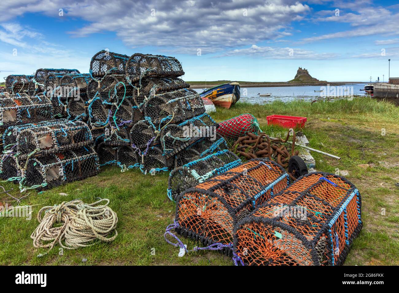 Lobster pots on the shoreline at the harbour of Holy Island on the Northumberland coast. Lindisfarne Castle is in the background, beyond the harbour. Stock Photo