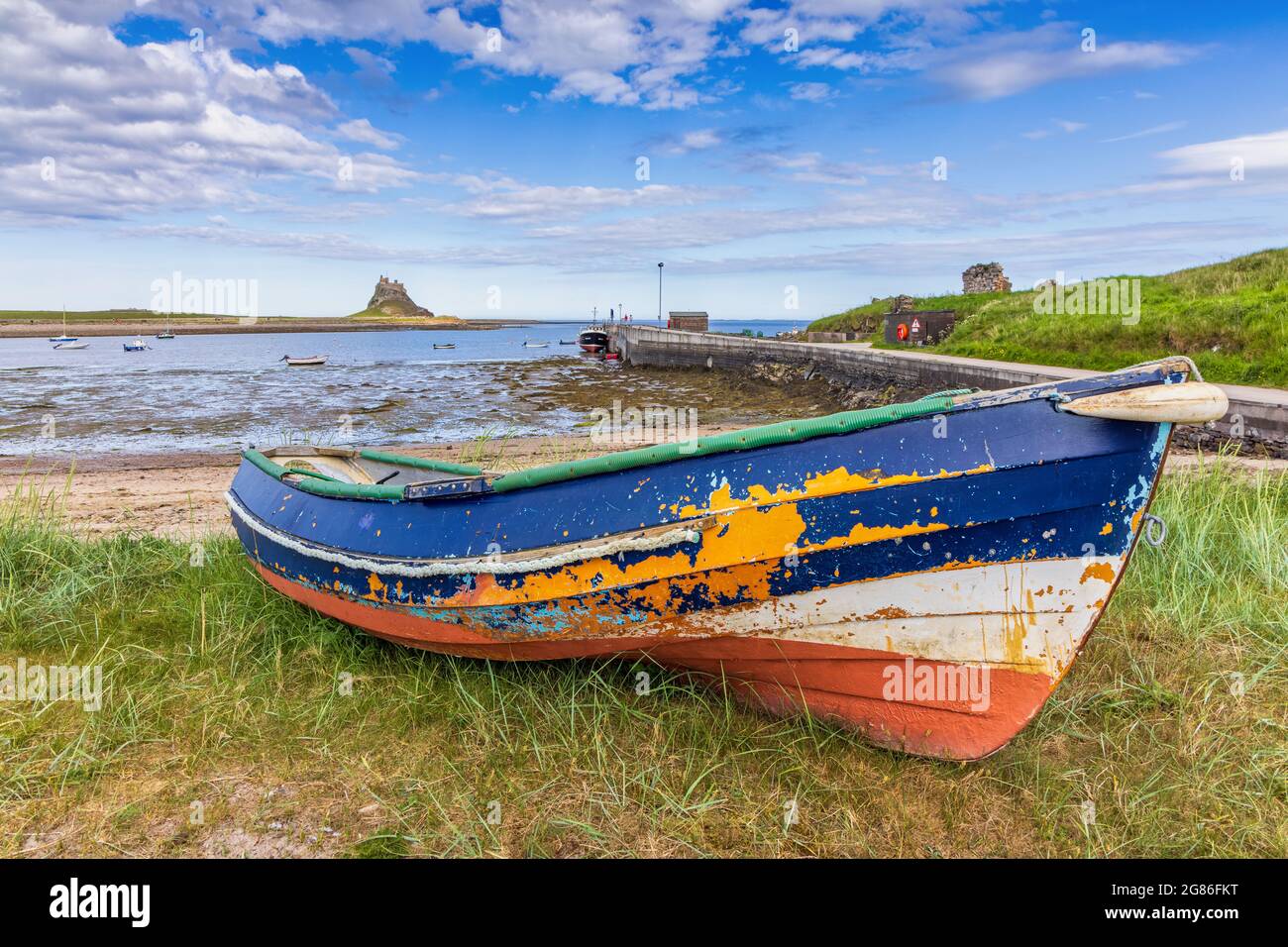 A colourful old fishing boat with flaking paint at Holy Island harbour in Northumberland, with Lindisfarne Castle in the distance.harbour Stock Photo