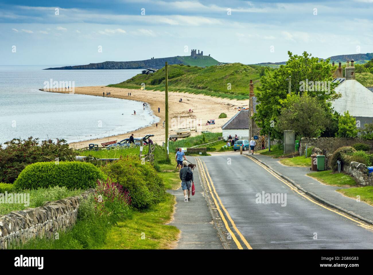 Road down to the village and beach at Low Newton-on-the Sea in Northumberland, with Dunstanburgh Castle in the distance. Stock Photo