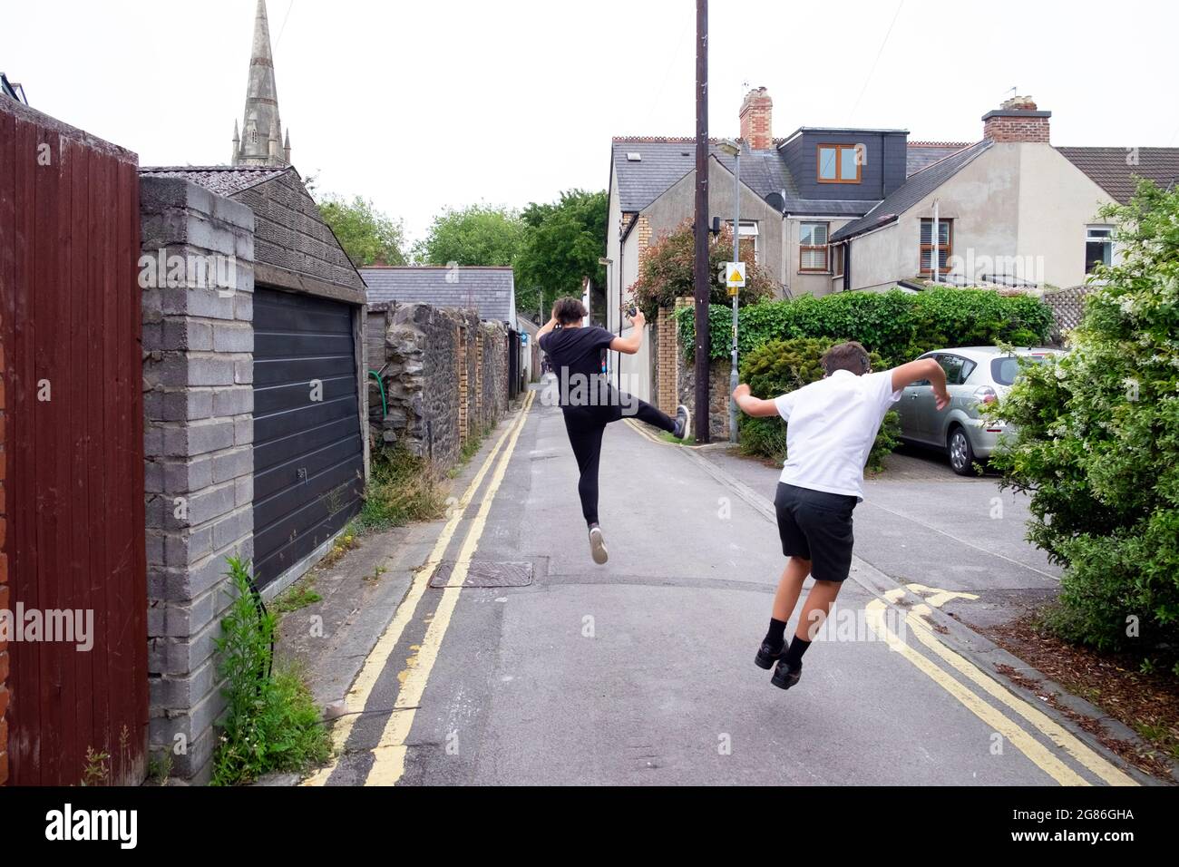 Happy childreh boys brothers rear back view hop skip jump click heels in elation running through a street alley in Cardiff Wales UK 2021 KATHY DEWITT Stock Photo