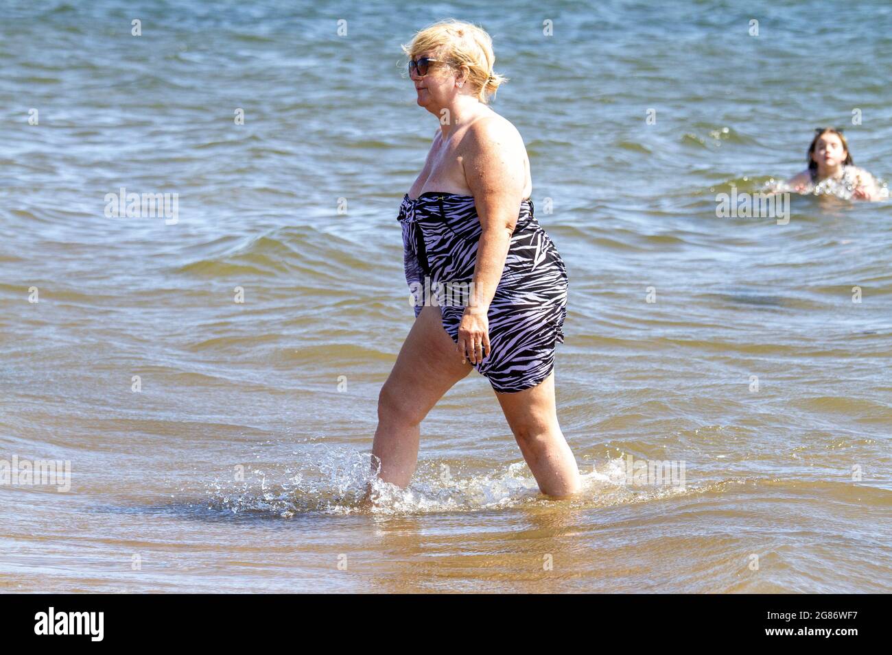 Dundee, Tayside, Scotland, UK. 17th July, 2021. UK Weather: July heatwave sweeping across North East Scotland with maximum temperature 27°C. Beach-goers day out at Broughty Ferry beach in Dundee. A local senior woman enjoying the warm summer sunshine cooling down in the river Tay. Credit: Dundee Photographics/Alamy Live News Stock Photo