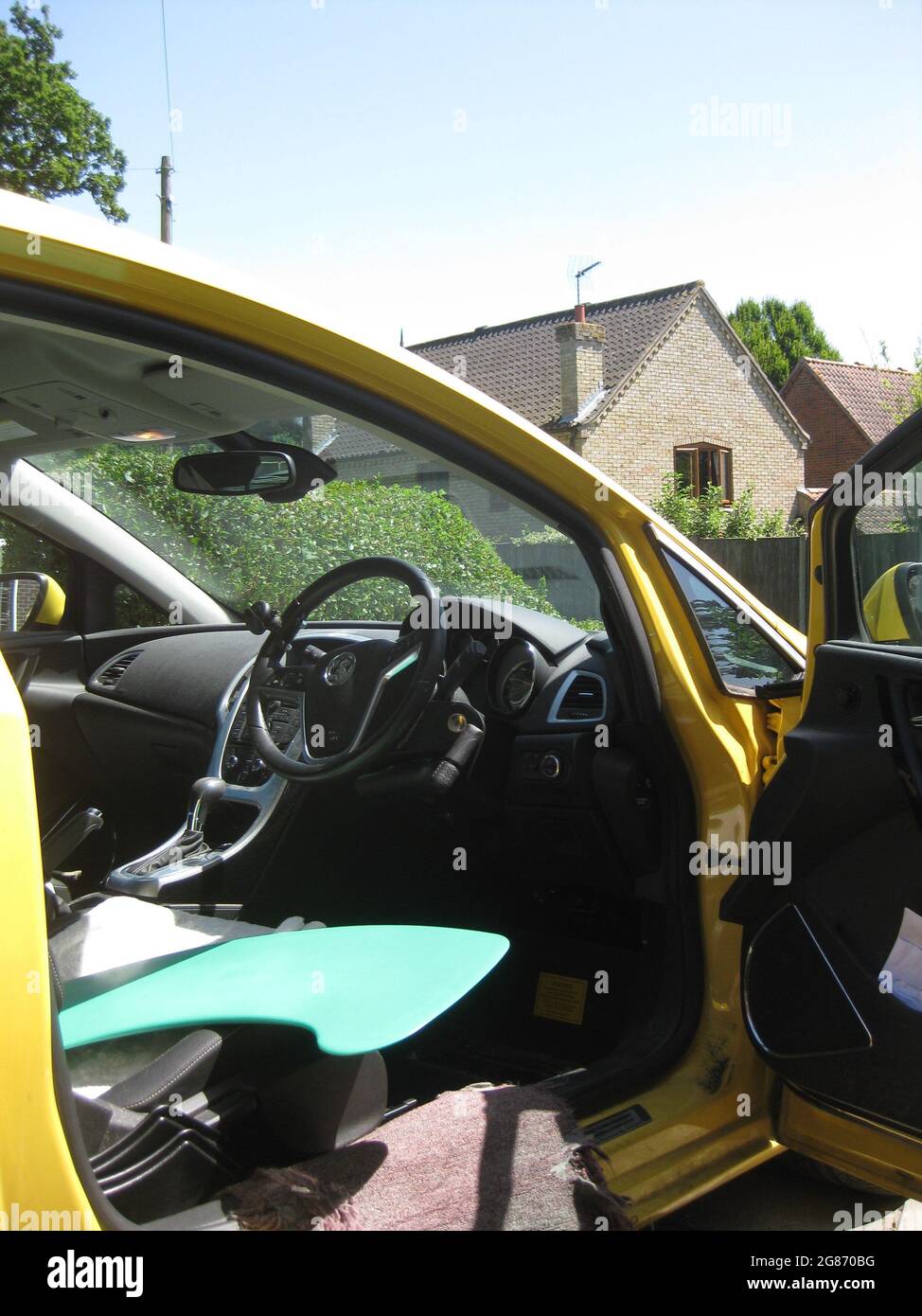 Modified car for disabled driver with steering aid, throttle and brake adaptation,  pedals blanking plate fitted and blue transfer board on seat Stock Photo