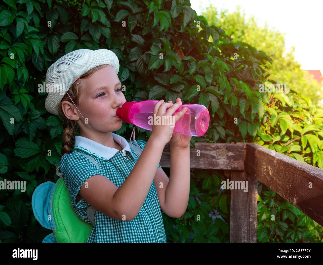 https://c8.alamy.com/comp/2G877CY/cute-school-little-girl-drinks-water-from-reusable-pink-bottle-outdoor-child-in-hat-enjoys-fresh-cold-water-on-green-summer-street-body-rehydration-2G877CY.jpg