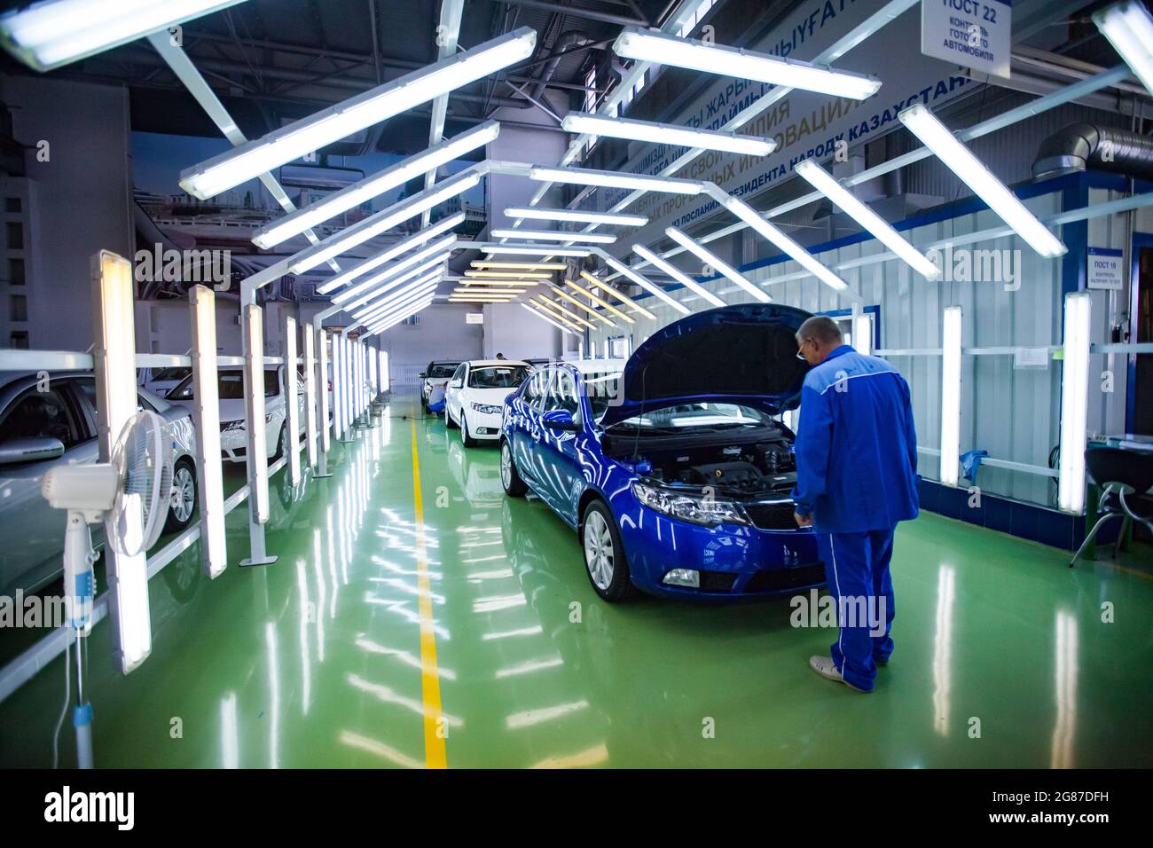 Ust'-Kamenogorsk, Kazakhstan: Asia-Auto company auto-building plant. Worker checking painting quality in light tunnel. White car in focus. Stock Photo