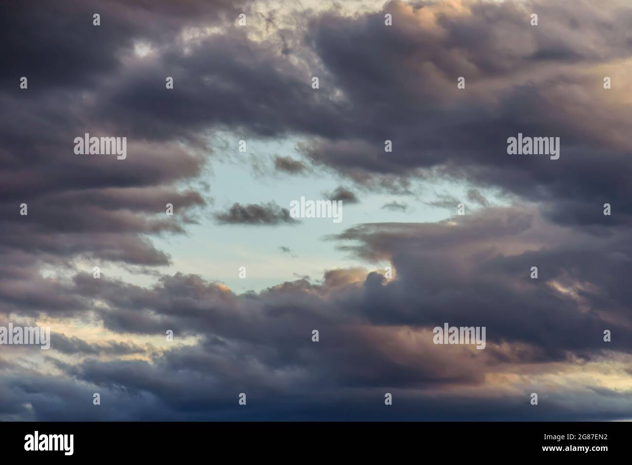 Stormy clouds with blue sky hole during sunset. Stock Photo