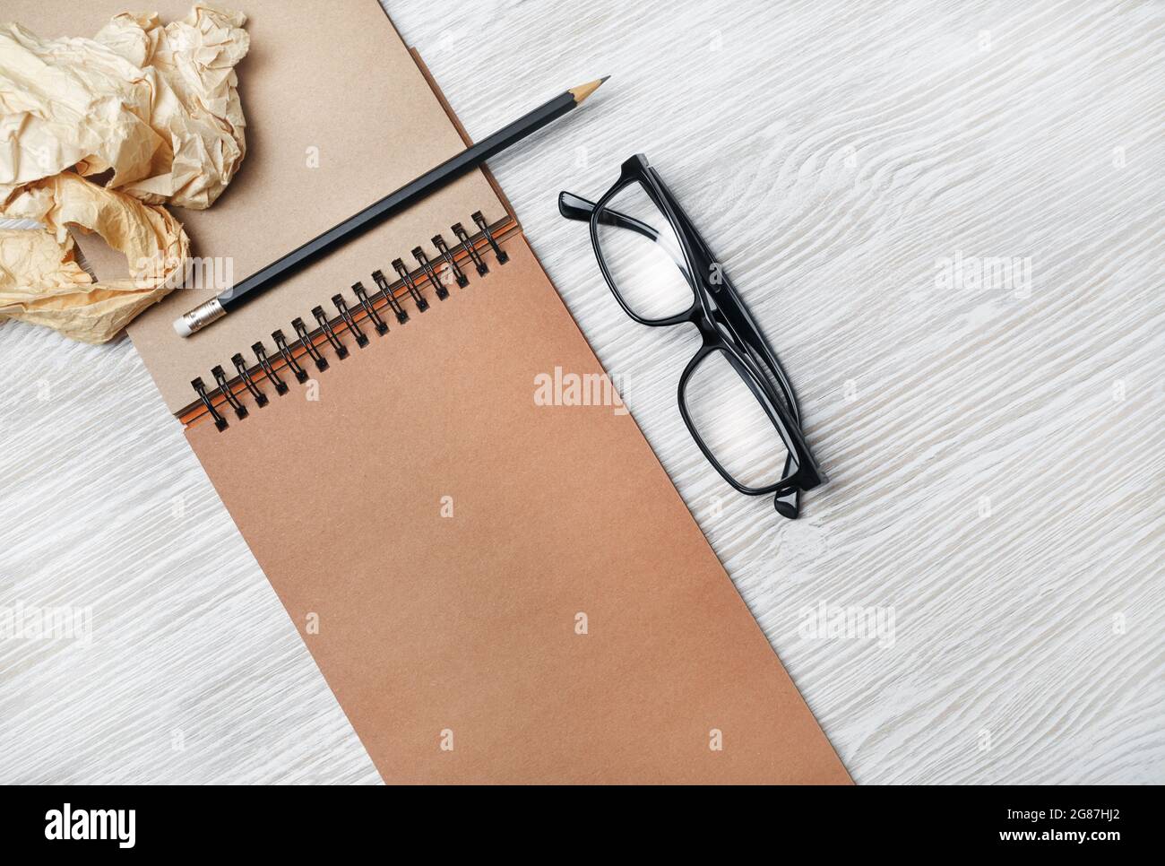 Photo of vintage notepad, glasses, pencil and crumpled paper on light