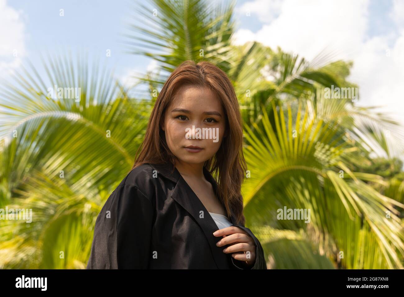 A South Asian young female wearing a black formal coat seriously posing in the park Stock Photo