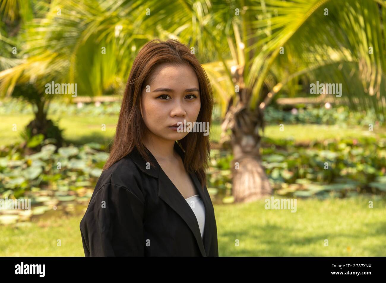 A South Asian young female wearing a black formal coat seriously  posing in the park Stock Photo