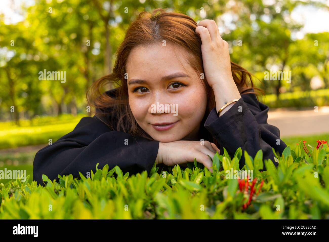 An attractive South Asian female wearing a black formal coat hiding among flowers in the park Stock Photo