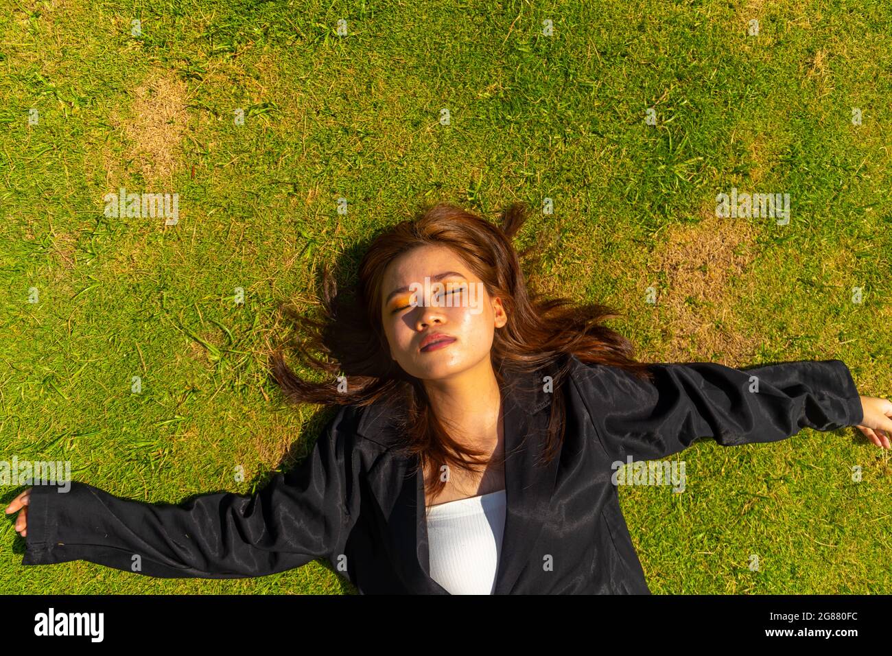 An attractive South Asian female wearing a black formal coat while lying on the ground Stock Photo