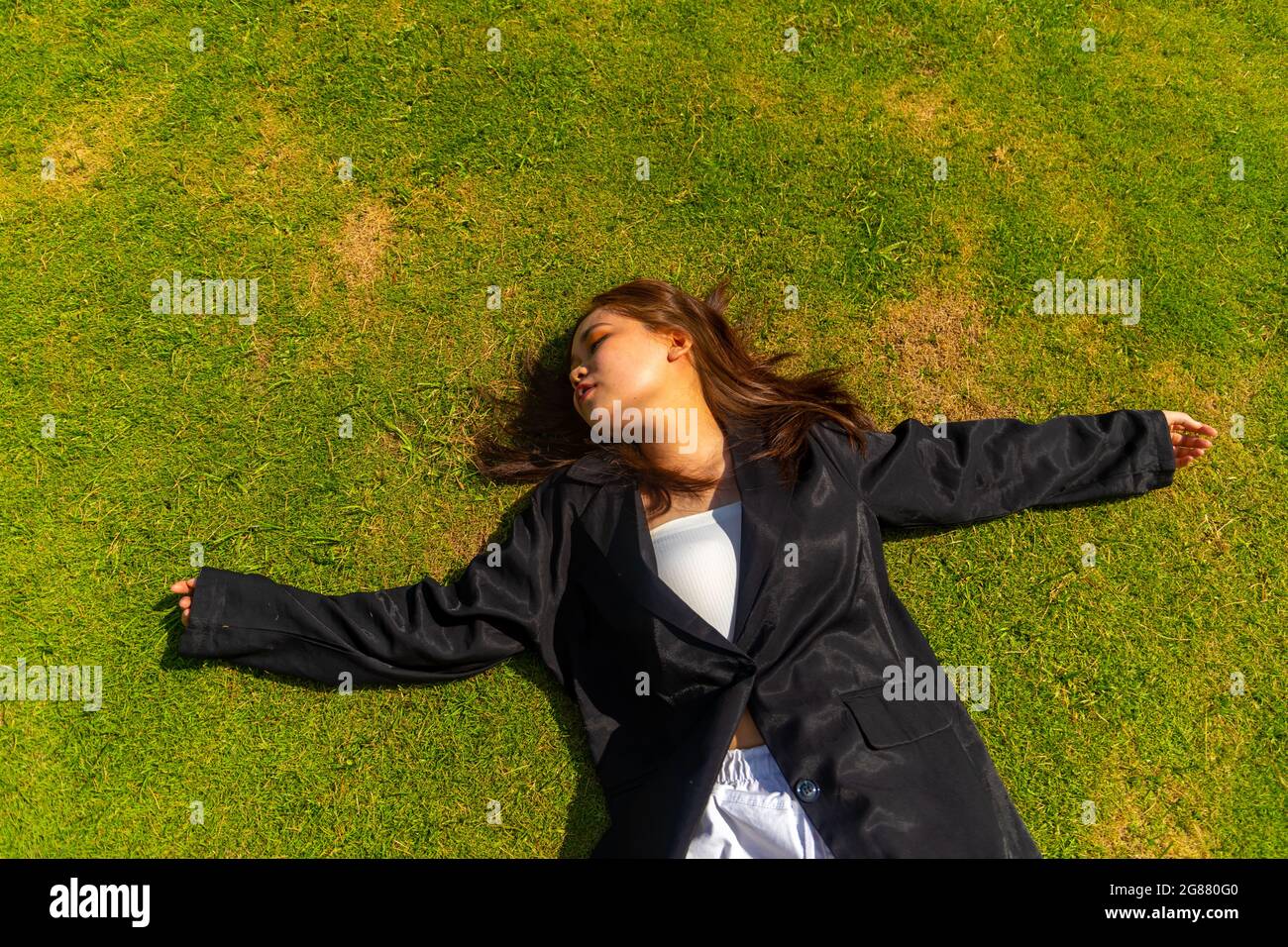 An attractive South Asian female wearing a black formal coat while lying on the ground Stock Photo