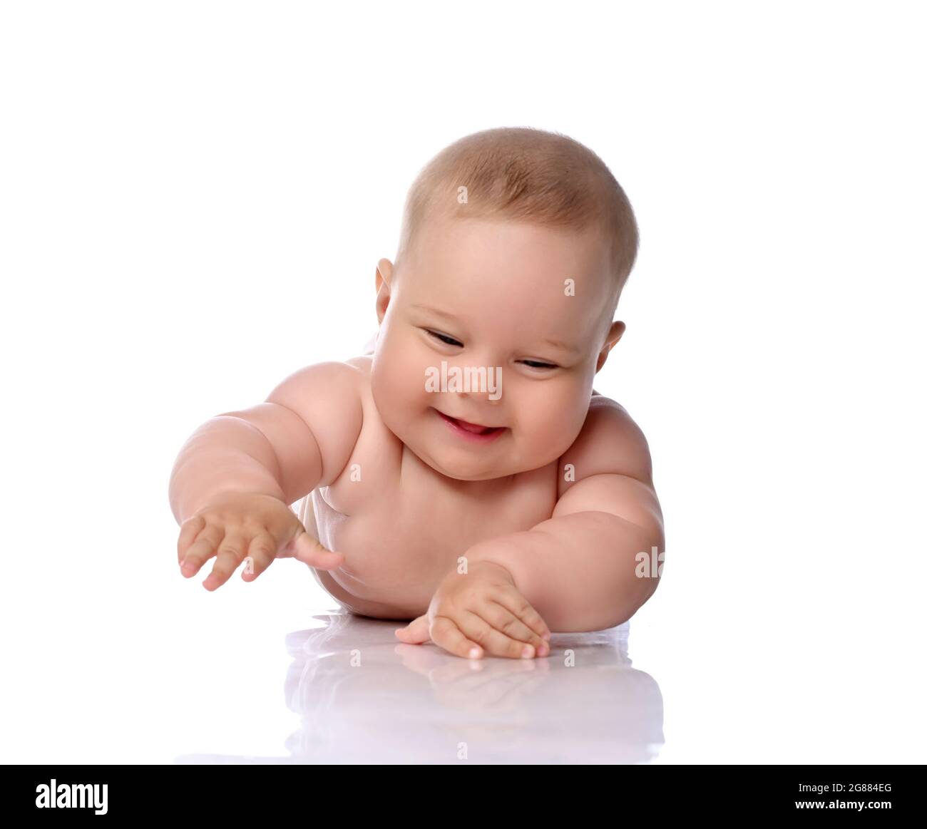 Smiling, laughing infant child baby girl kid in diaper is lying on her tummy holding hand up, slapping on floor  Stock Photo