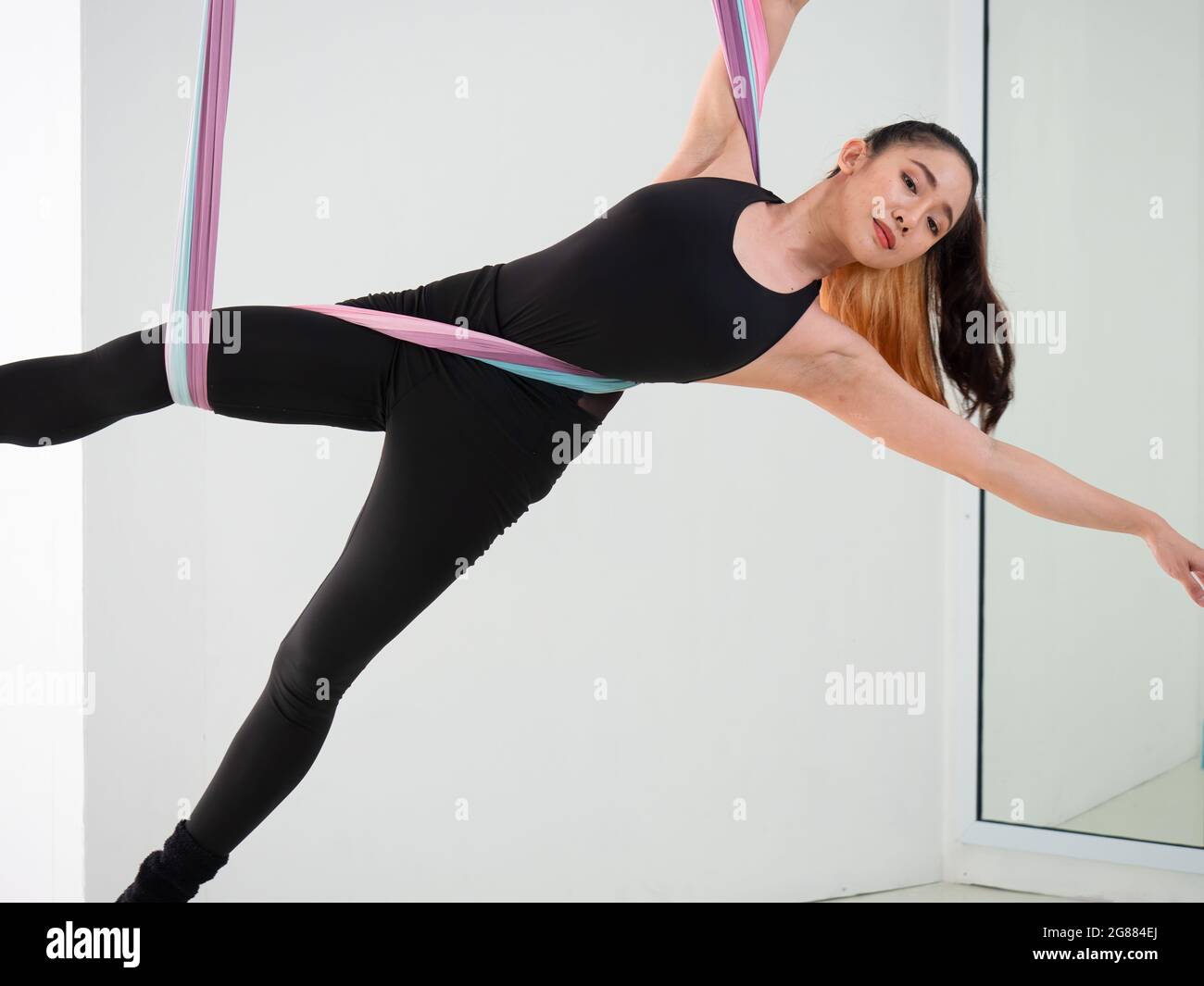 Young beautiful Asian dancer dressed in black color performing aerial dance with multi-color fabrics in the studio. Stock Photo
