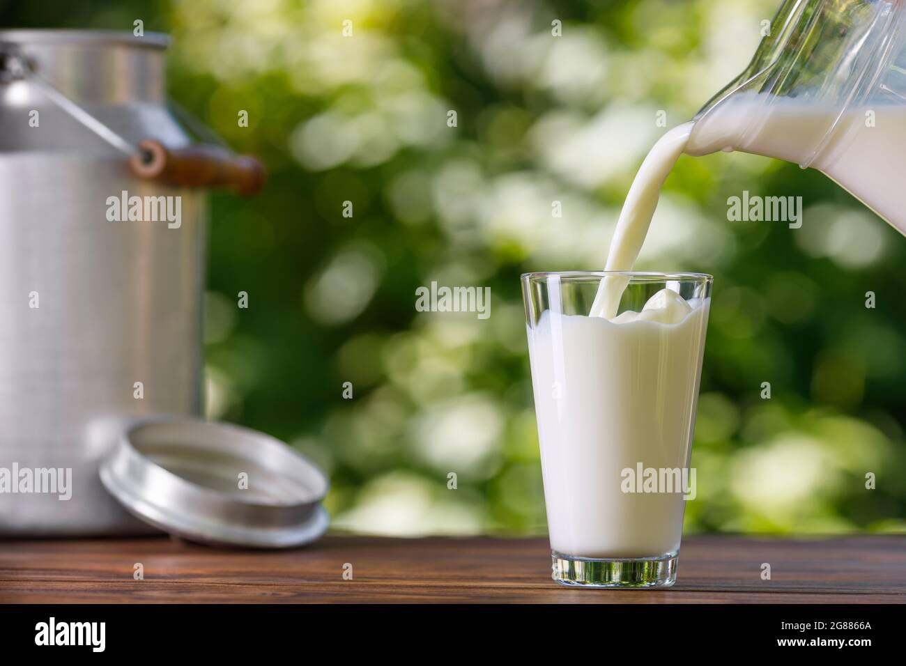 milk pouring from jug into glass outdoors Stock Photo