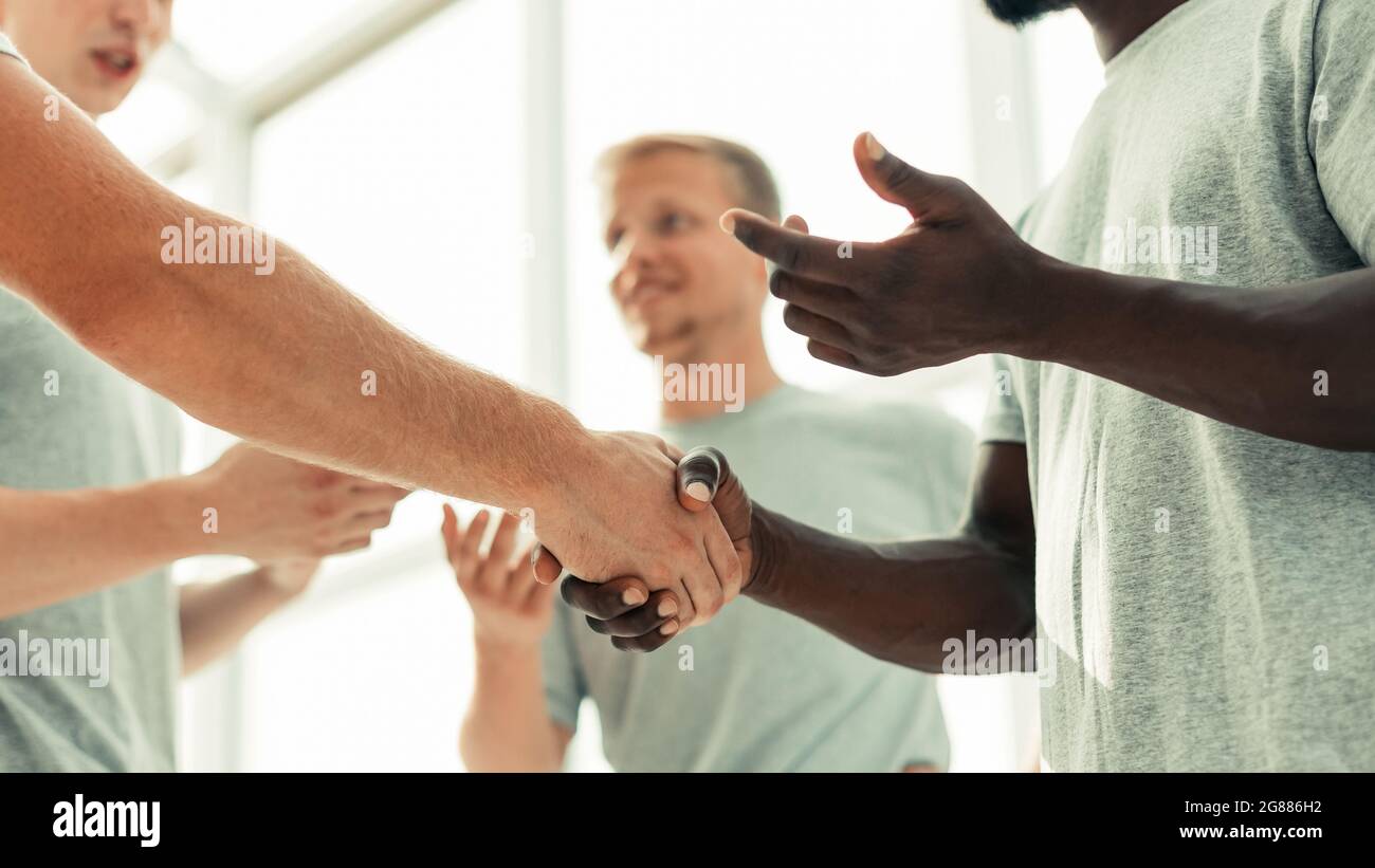close up. two comrades shaking hands, standing in a circle of friends ...