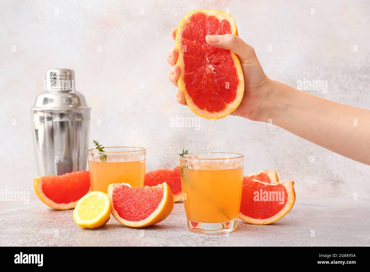 Woman squeezing grapefruit into glass on light background Stock Photo