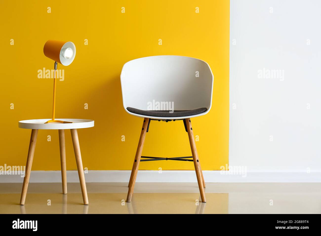 Modern armchair and lamp on table near color wall Stock Photo - Alamy