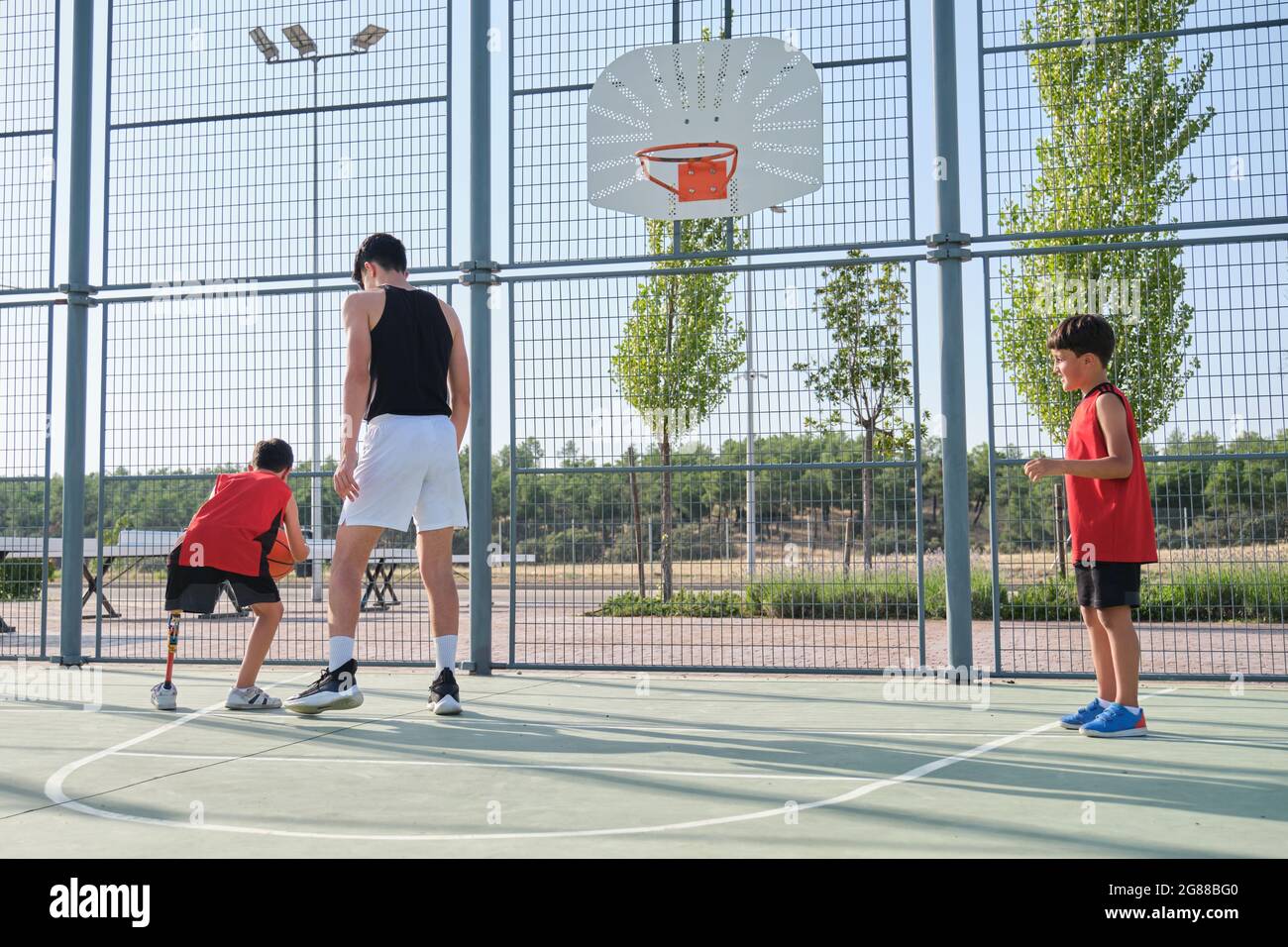 Basketball trainer playing basketball with two children, one of them has a  leg prosthesis. Coach training two kids Stock Photo - Alamy