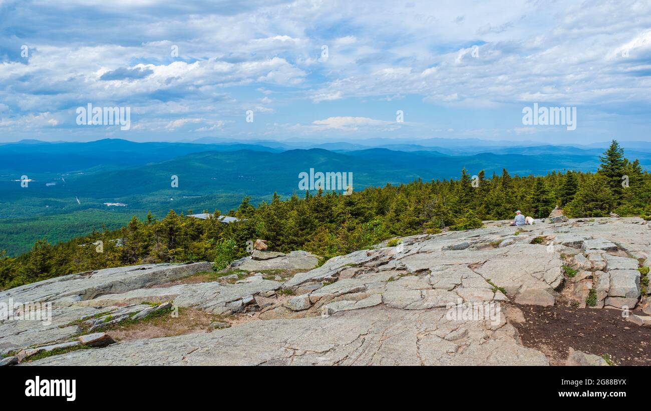 Northern view from Mt. Kearsarge summit towards Ragged Mountain. Hikers relaxing on the rocky outcrop. Stunted spruce trees. Distant peaks and ridges. Stock Photo