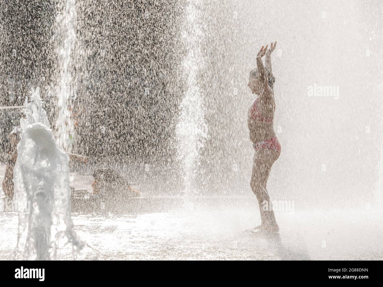 Silhouette of a girl standing with her hands high in water fountain ...