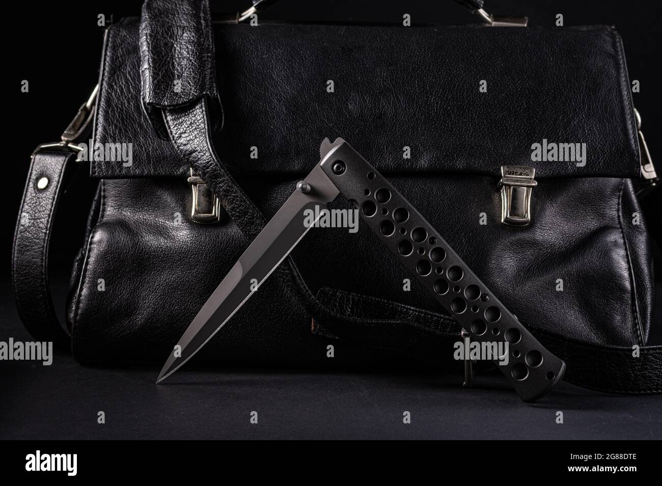 Large folding knife on the background of a leather briefcase. Bent knife and leather briefcase