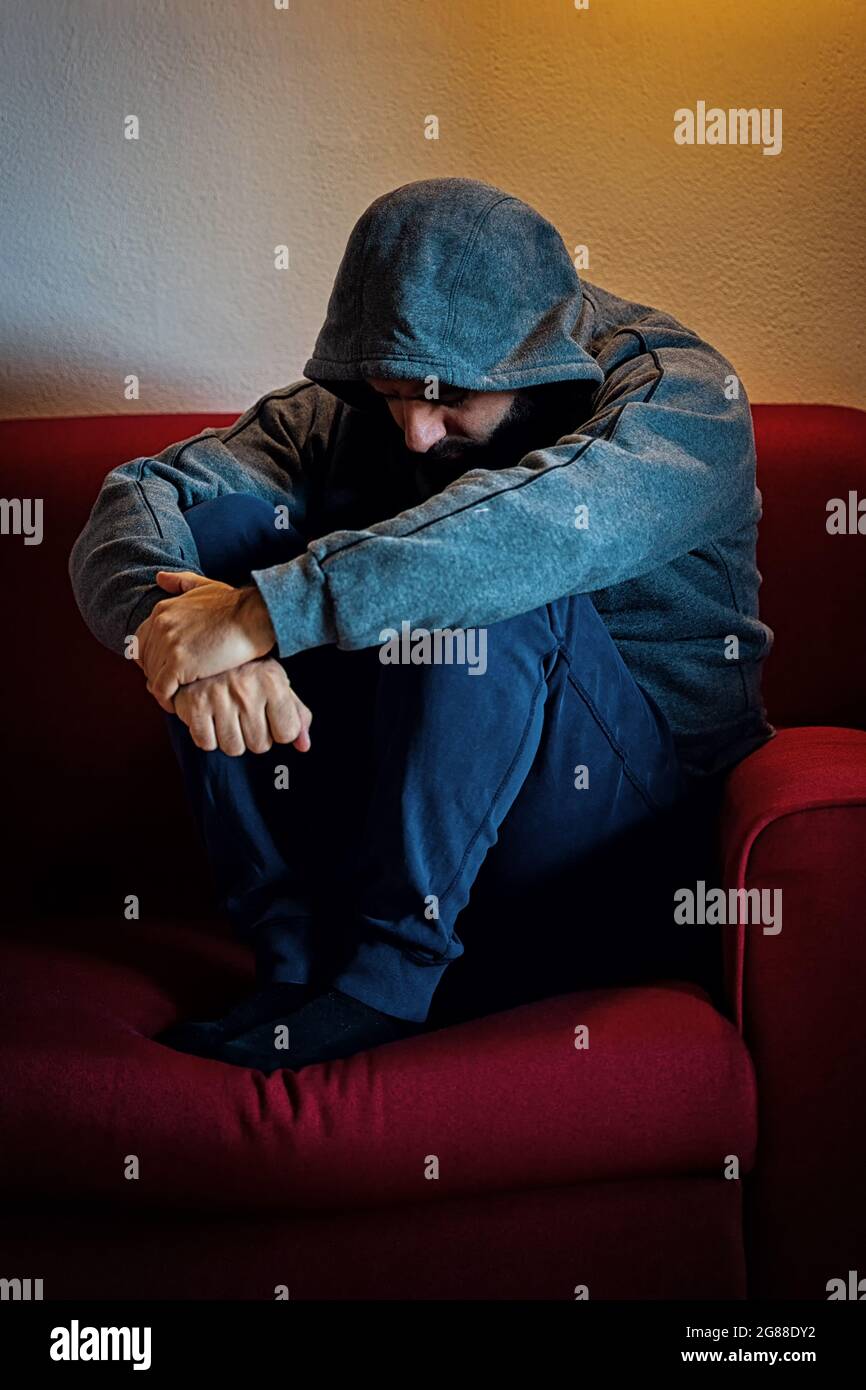 Depressed man, with hood on his head, sitting alone on a sofa Stock ...
