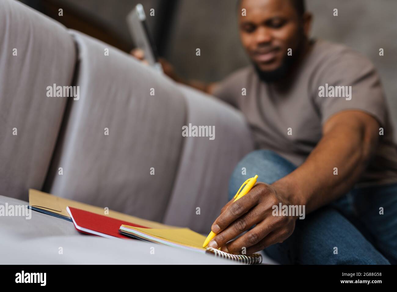 Black unshaven man using tablet computer while writing down notes at home Stock Photo