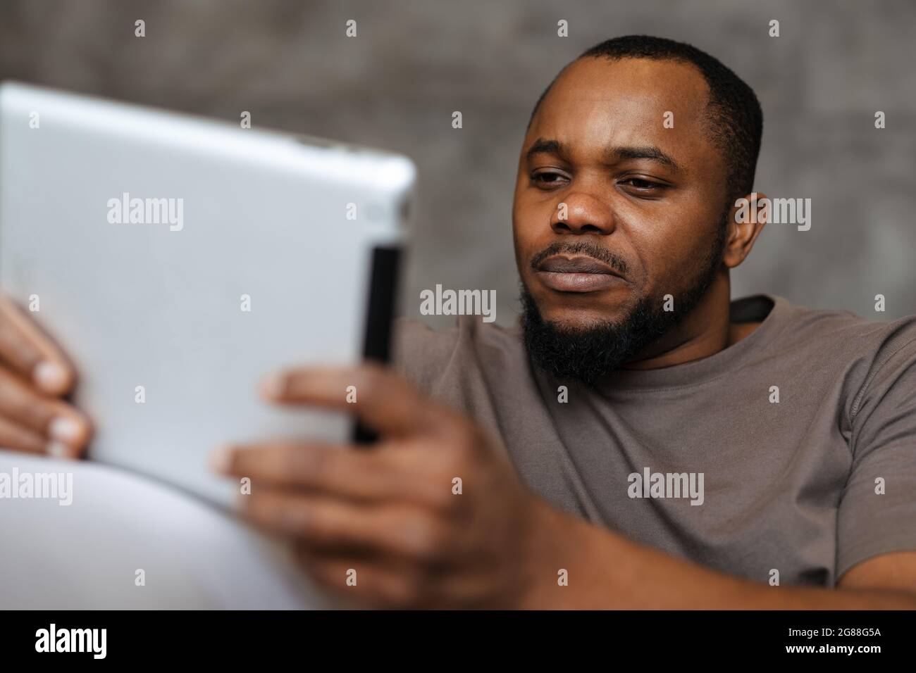 Black unshaven man using tablet computer while sitting on sofa at home Stock Photo