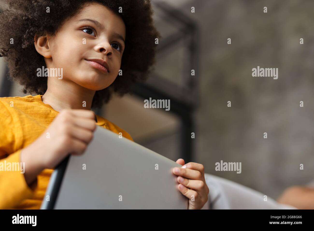 Black curly boy using tablet computer while sitting on sofa at home Stock Photo