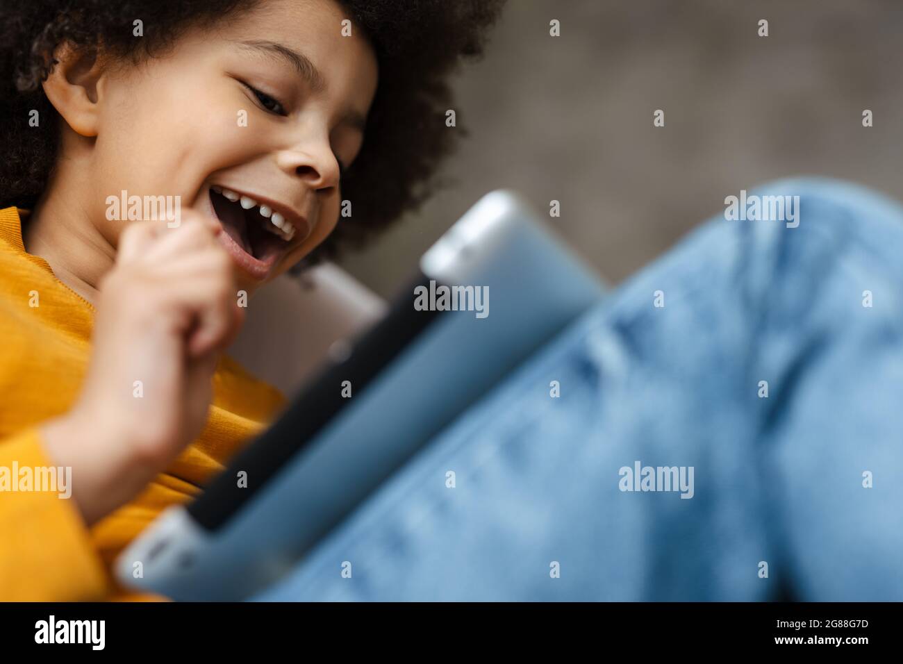 Black curly boy smiling and using tablet computer while sitting on sofa at home Stock Photo