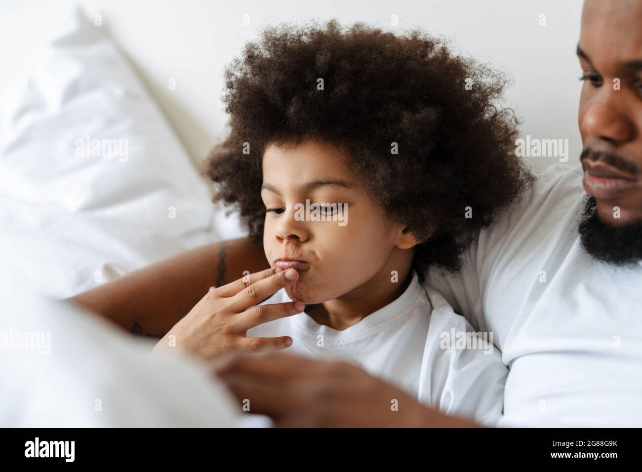 Black father and son using tablet computer while lying in bed at home Stock Photo
