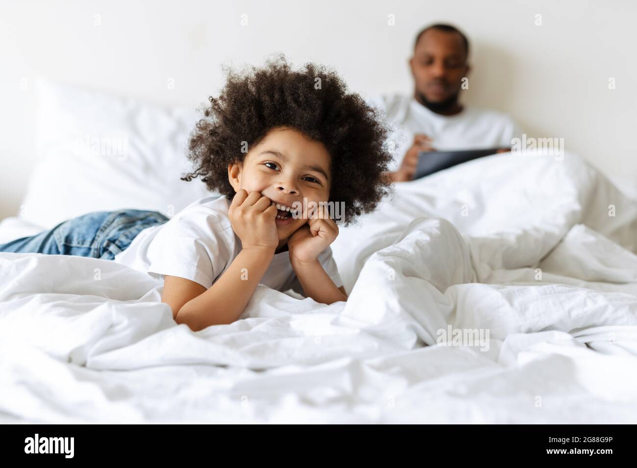 Black boy laughing while his father using tablet computer in bed at home Stock Photo