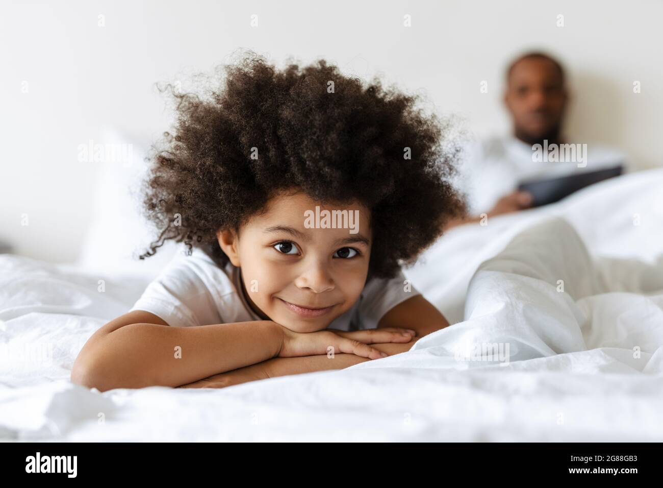 Black boy smiling while his father using tablet computer in bed at home Stock Photo